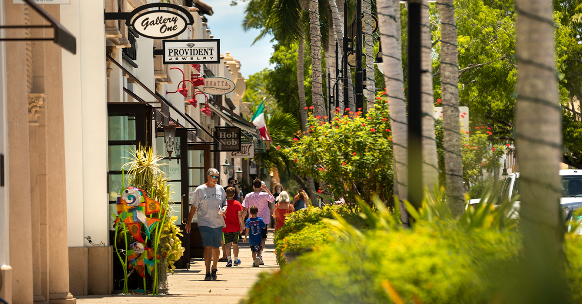 People walking along a palm-lined shopping street with boutiques.