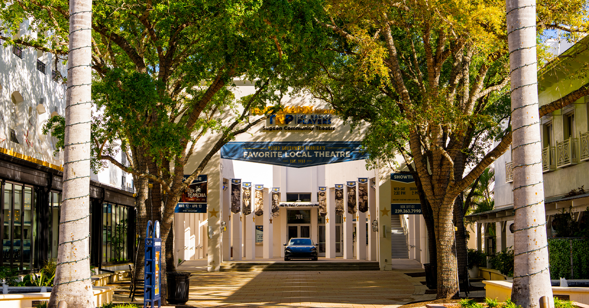 A tree-lined walkway leads to a local theatre entrance with banners and signage.