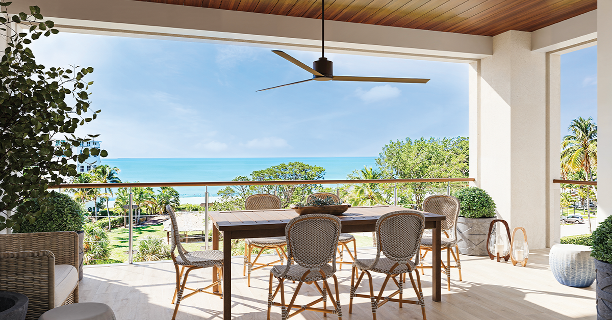 Covered terrace with dining table and ocean view beyond palm trees.
