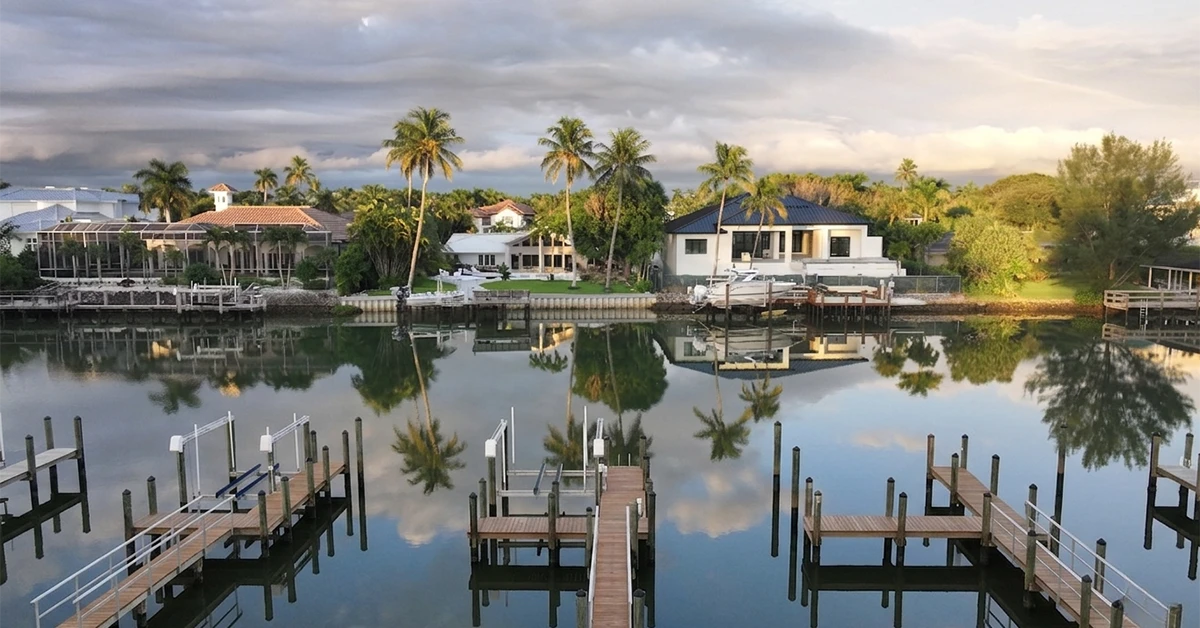 Waterfront homes with private docks and palm trees reflected in calm bay at sunset